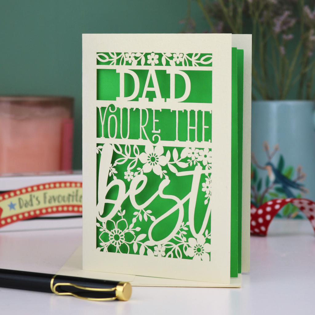 Laser cut Father's Day Card with 'Dad, you're the best' text on a table with decorative items in the background