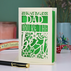 Laser cut Father's Day Card with 'Dad, you're the best' text on a table with decorative items in the background