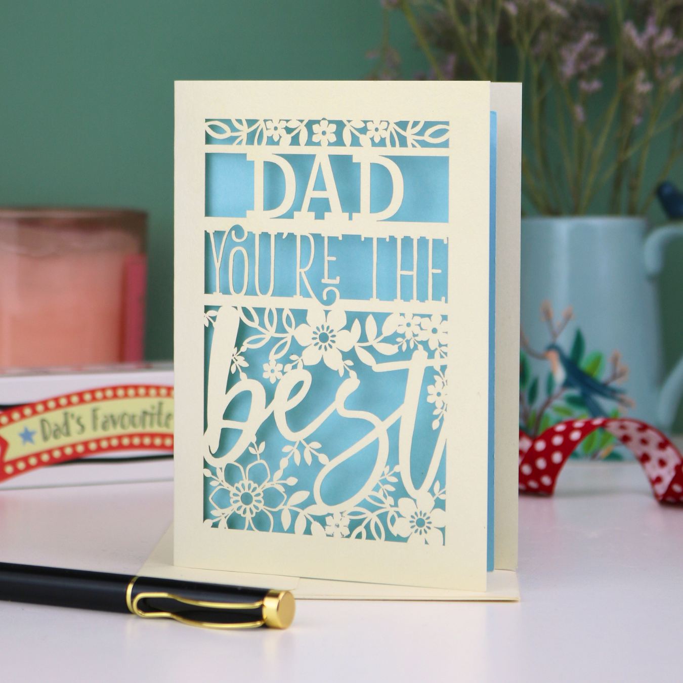 Unique Cut out Father's Day Card with 'Dad, you're the best' text on a table with decorative items in the background
