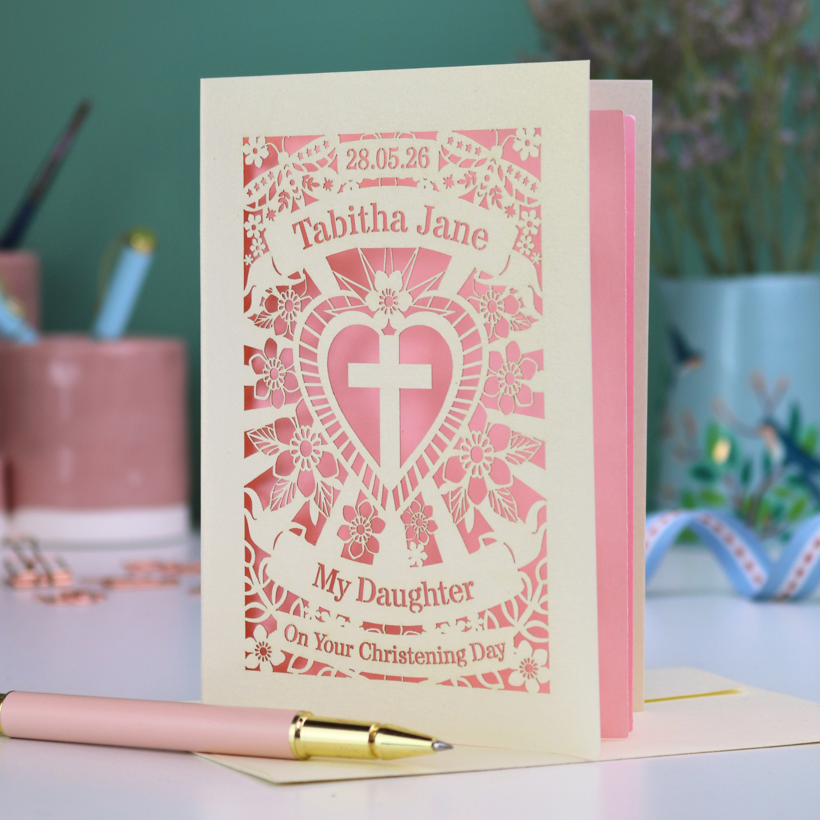 Personalized laser cut christening daughter card with decorative heart and cross design and text on a table.