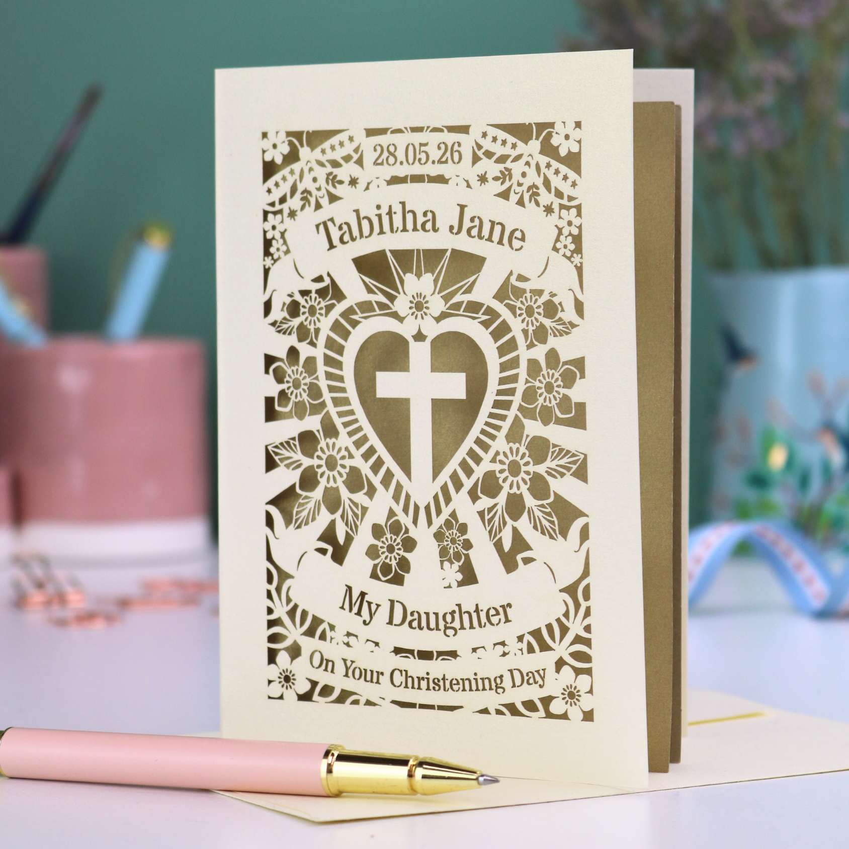 Personalized Daughter On Your Christening card with floral design and cross for a christening, placed on a desk with stationery items.