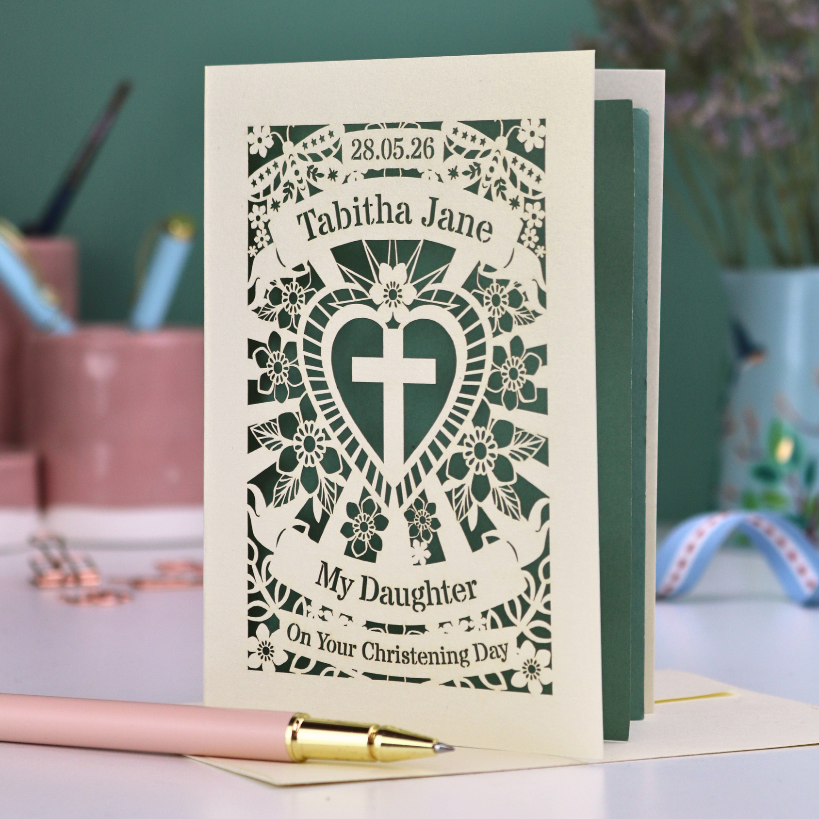 Personalized cut out Christening Daughter card with decorative design and text on a desk with stationery items.