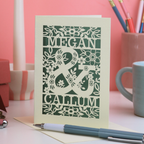 A laser cut engagement card on a pink background