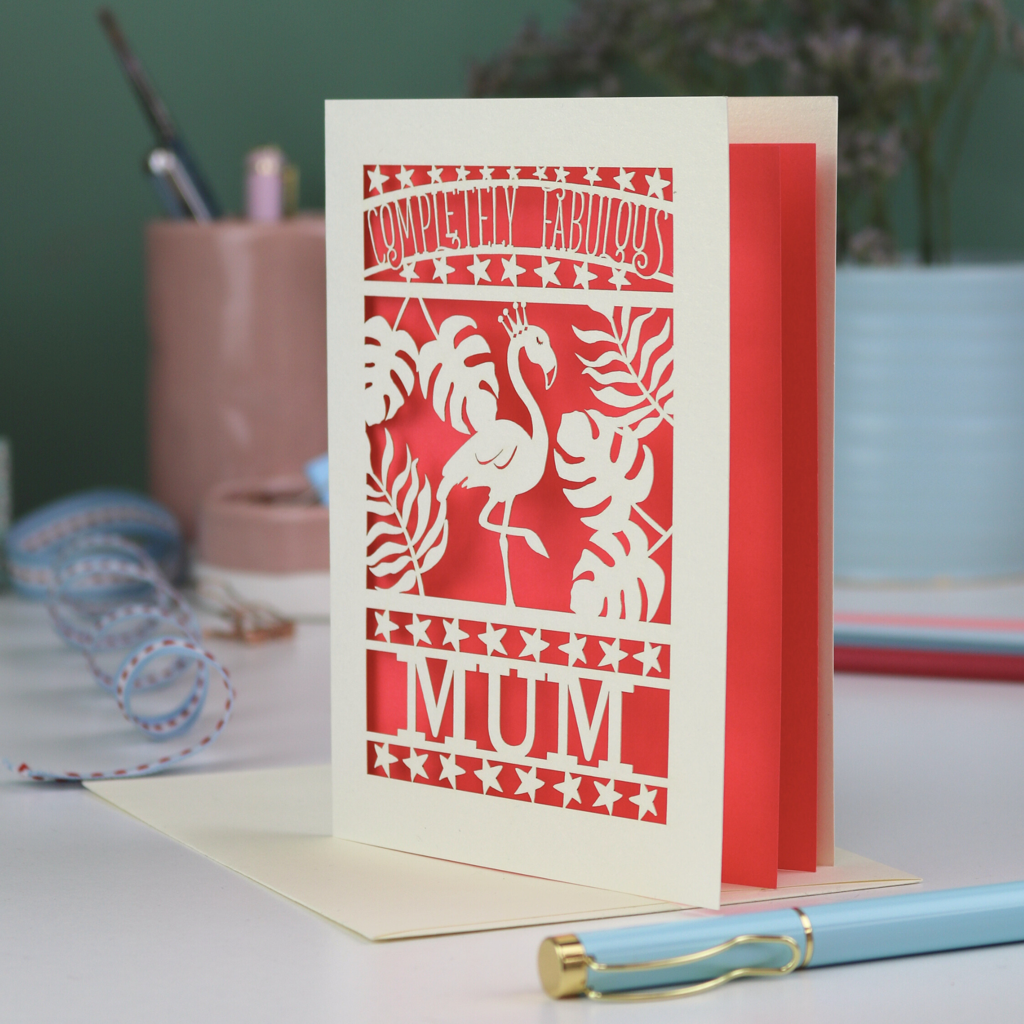 Greeting card with flamingo design and 'Completely Fabulous Mum' text on a desk with stationery items.