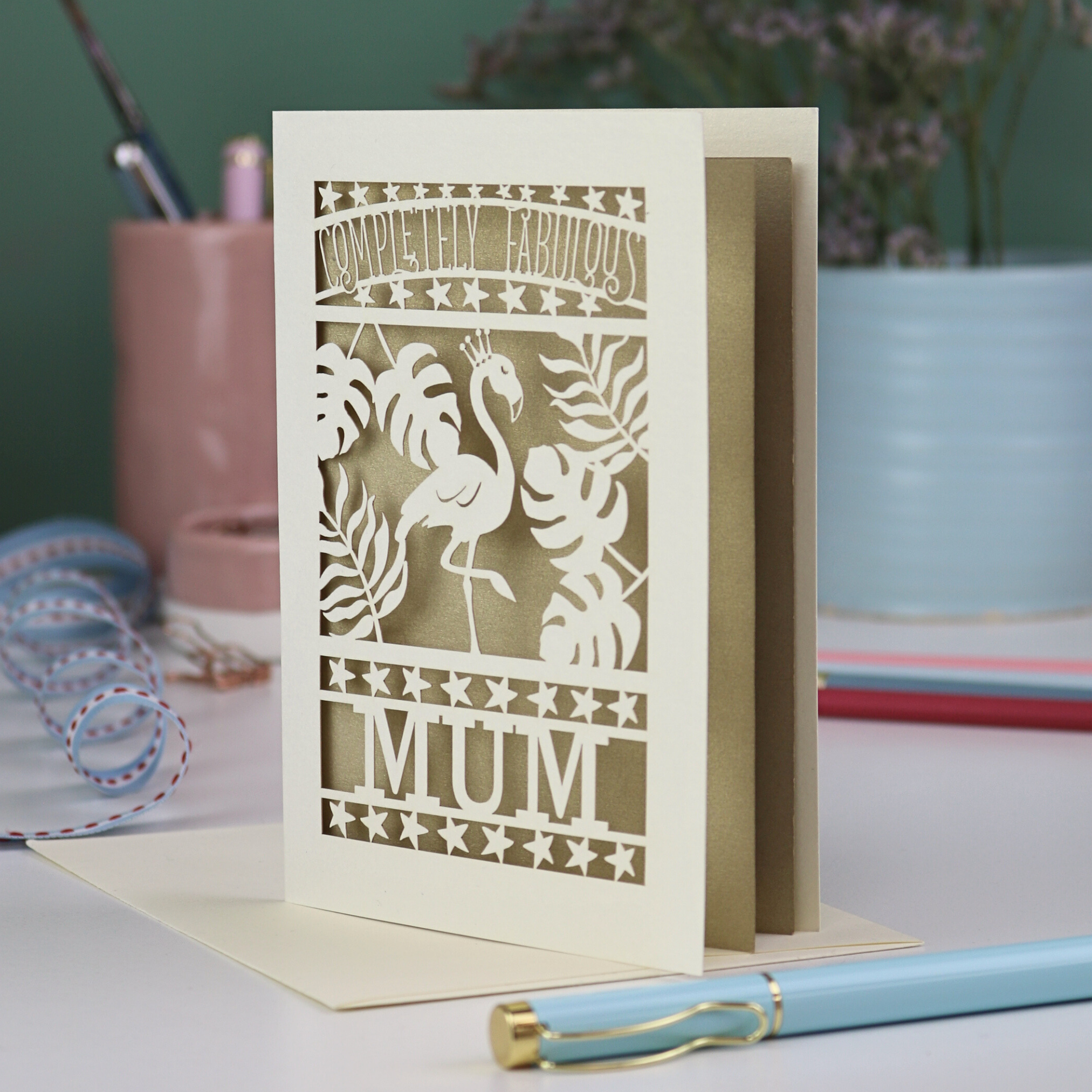 Greeting card with flamingo design and 'Completely Fabulous Mum' text on a desk with stationery items.