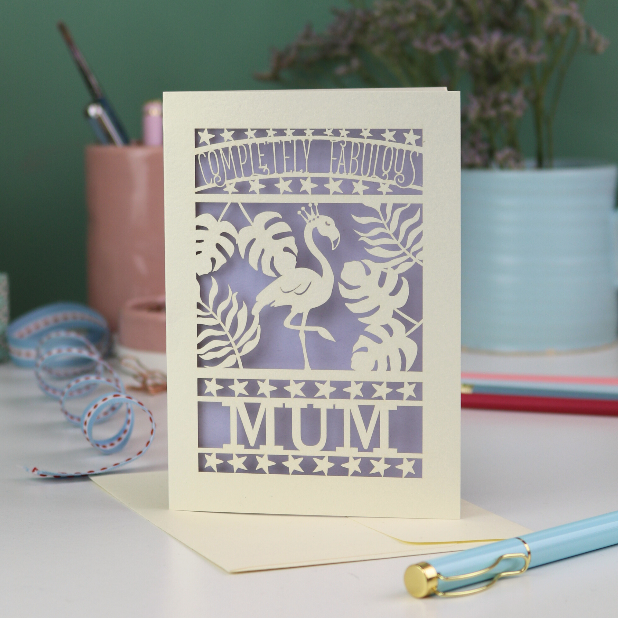 Laser-cut card with flamingo design and text on a desk with stationery items.