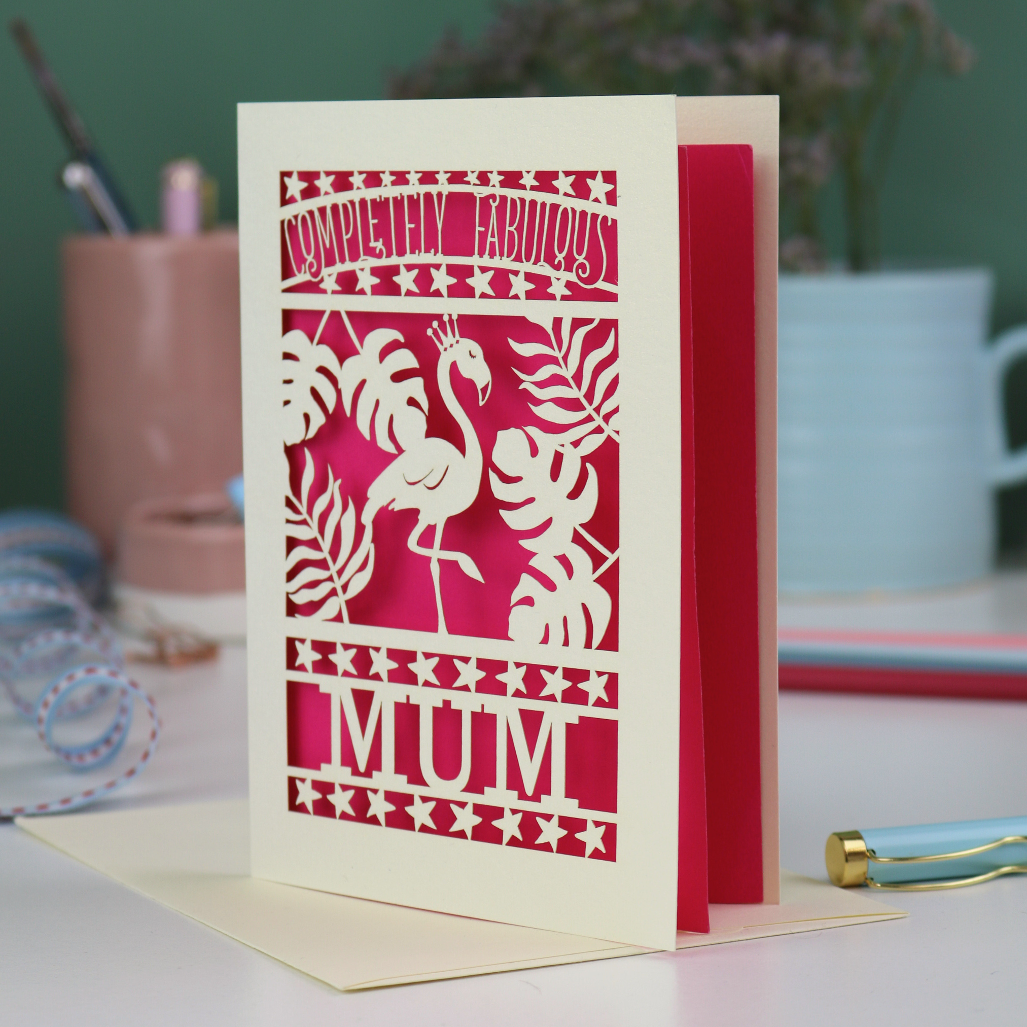Greeting card with flamingo design and 'Completely Fabulous Mum' text on a desk with stationery items.