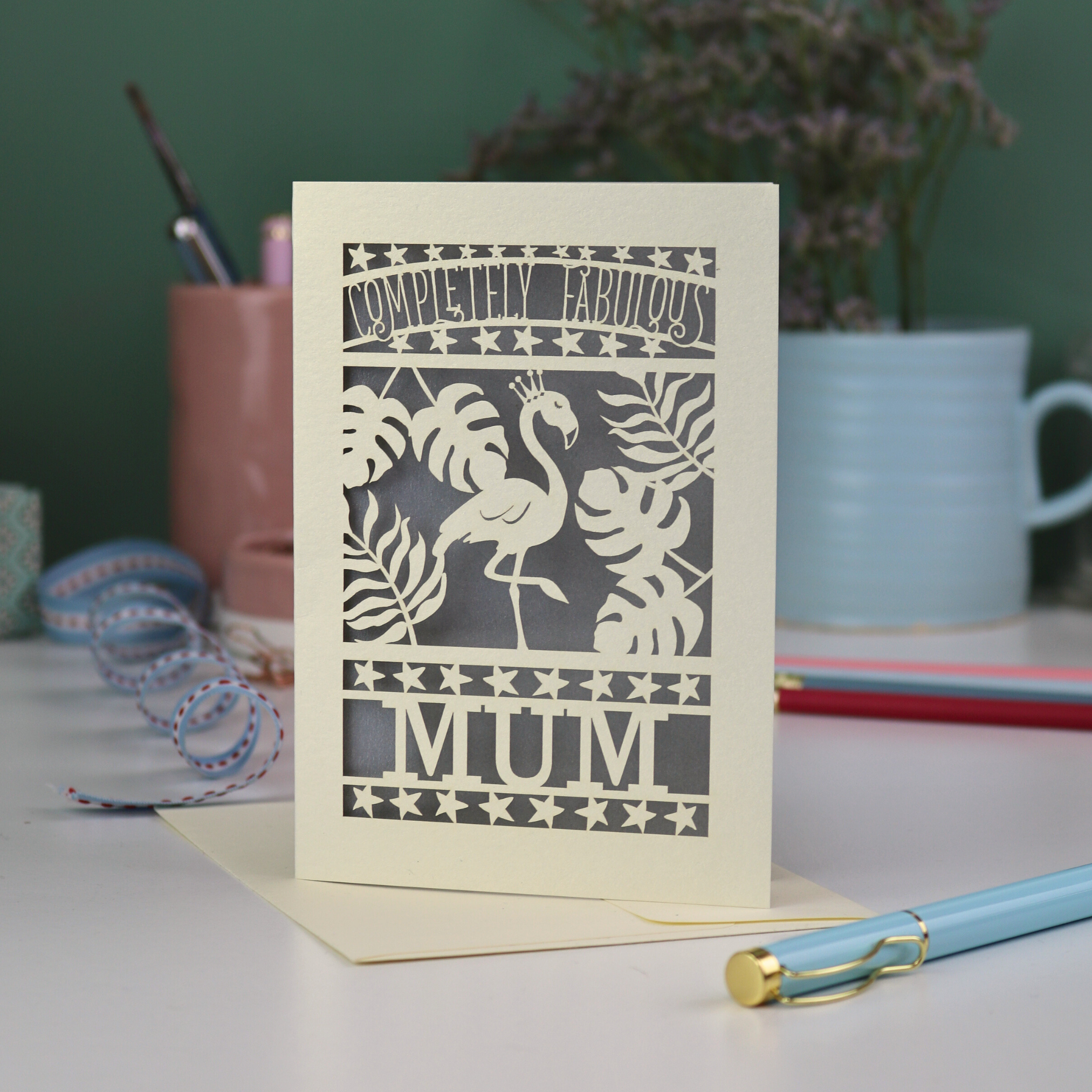 Greeting card with flamingo design and 'Completely Fabulous Mum' text on a desk with stationery items.