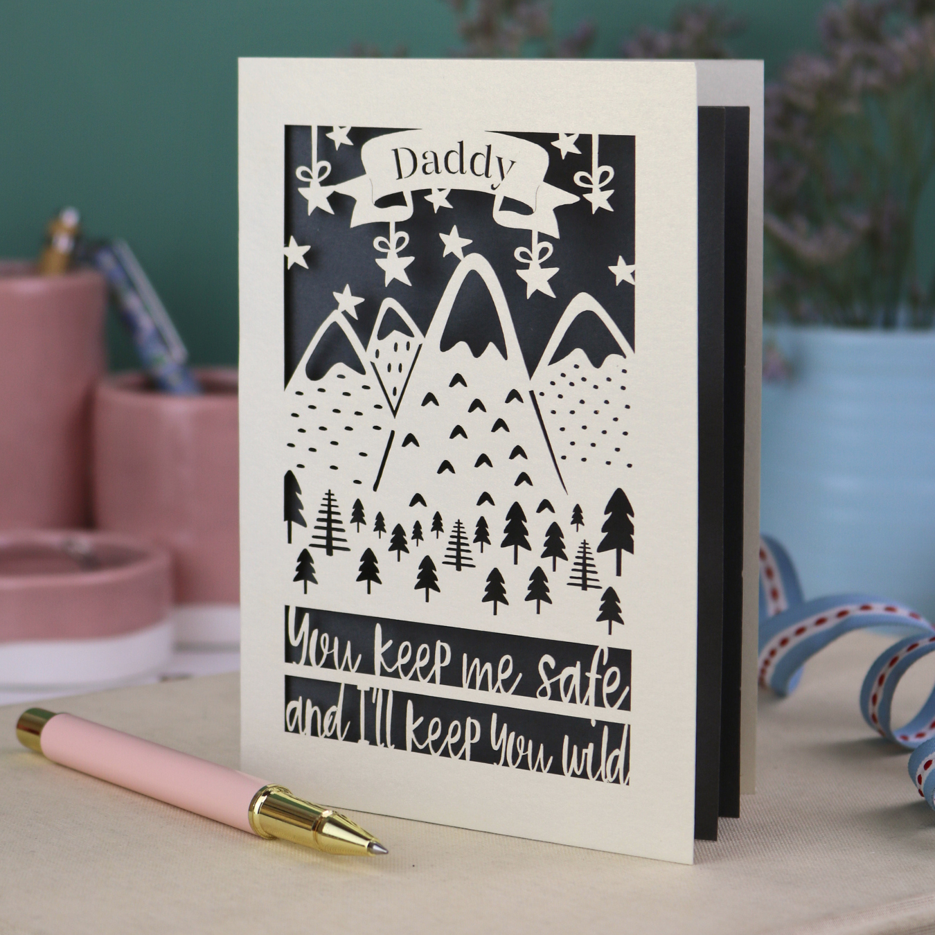 A cream laser cut personalised Father's Day card with mountain design and the text "Daddy" in a banner at the top, and "You keep me safe and I'll keep you wild" underneath