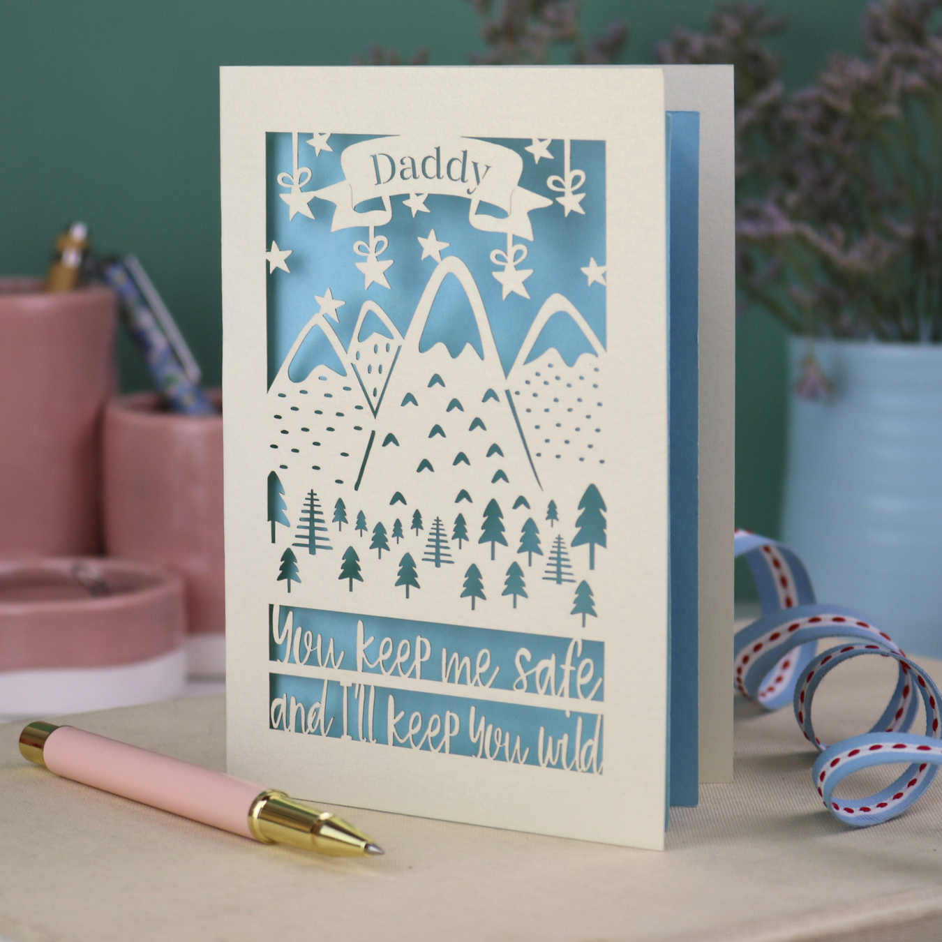A cream laser cut personalised Father's Day card with mountain design and the text "Daddy" in a banner at the top, and "You keep me safe and I'll keep you wild" underneath