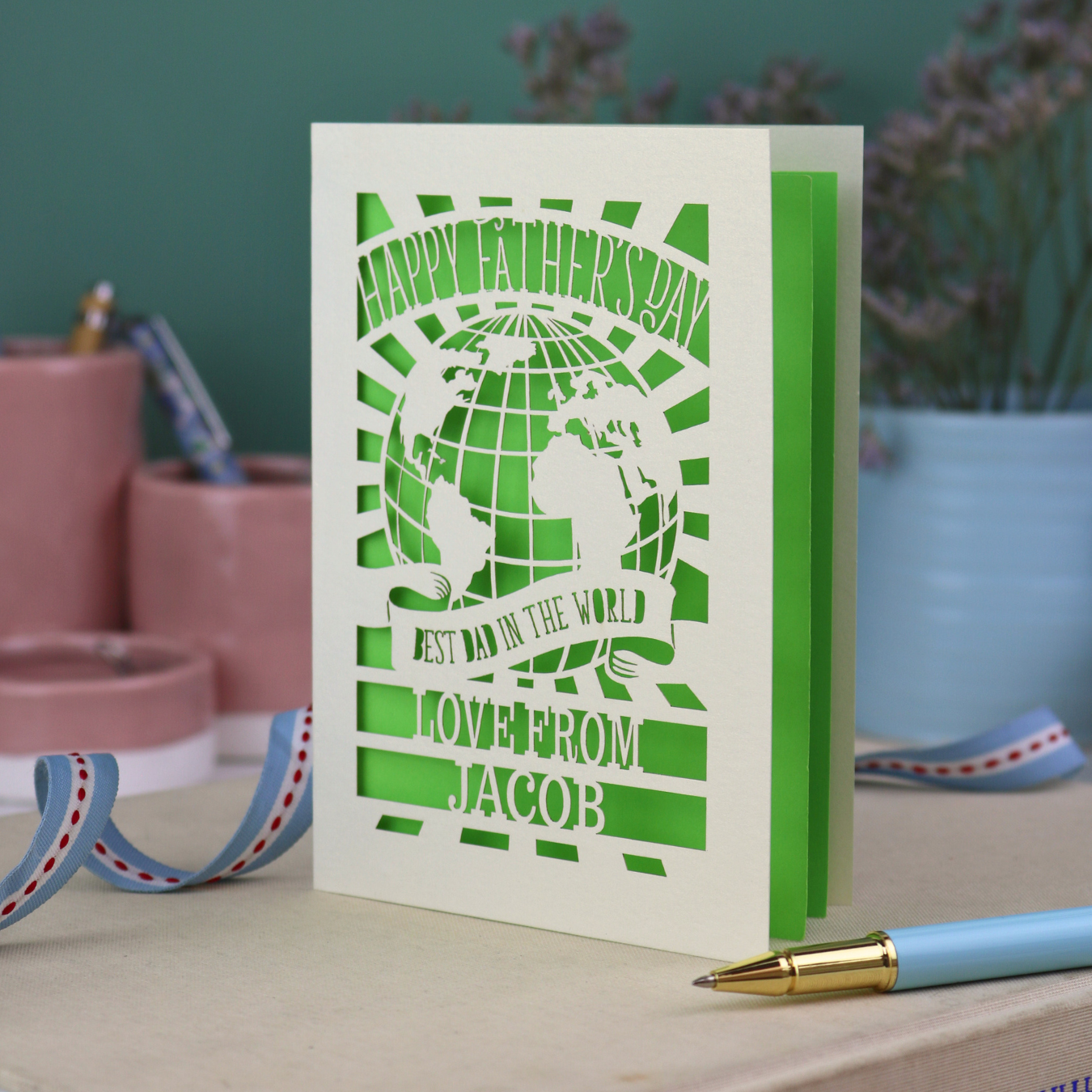 A laser cut Father's Day card with cream cut out card and a bright green paper insert. Card has a globe design and the text "Happy Father's Day to the best dad in the world, love from" and is personalised with a name. 