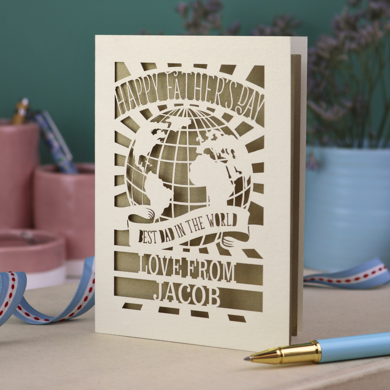 A laser cut Father's Day card with cream cut out card and a gold leaf paper insert. Card has a globe design and the text "Happy Father's Day to the best dad in the world, love from" and is personalised with a name. 