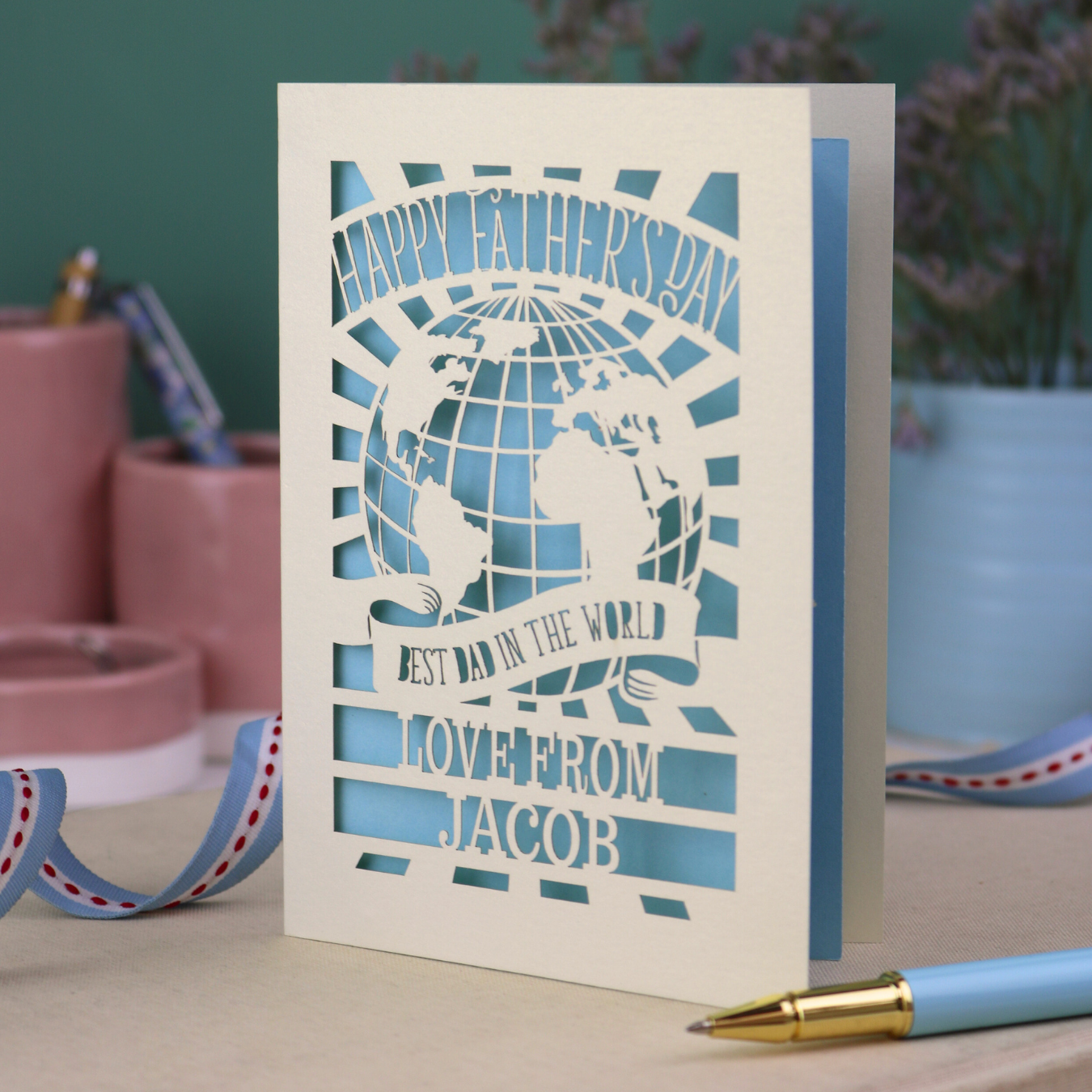 A laser cut Father's Day card with cream cut out card and a light blue paper insert. Card has a globe design and the text "Happy Father's Day to the best dad in the world, love from" and is personalised with a name. 