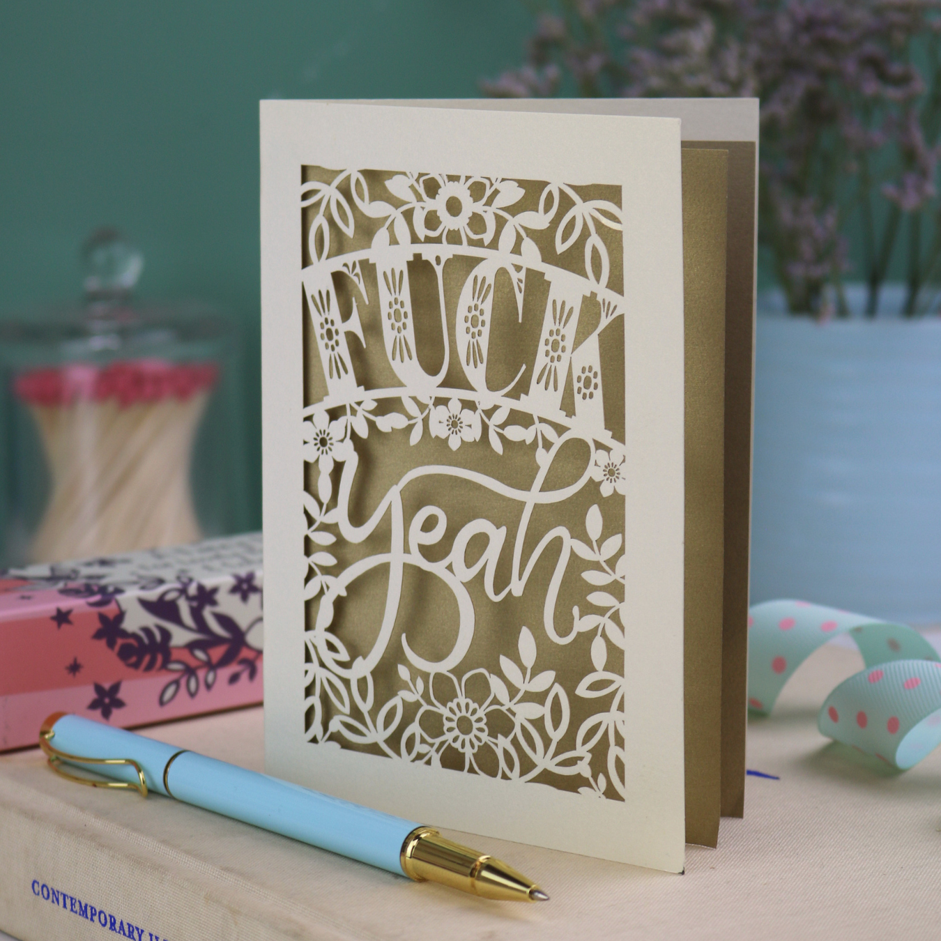 Funny laser cut congratulations Card with decorative, swearing text on a table with stationery items