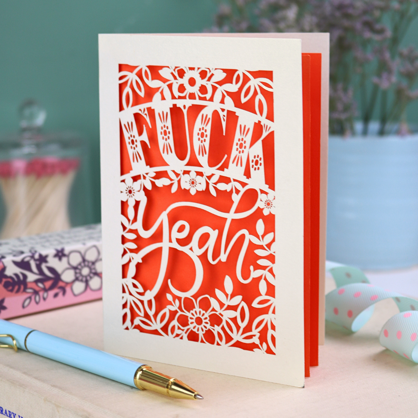 Funny laser cut congratulations Card with decorative, swearing text on a table with stationery items