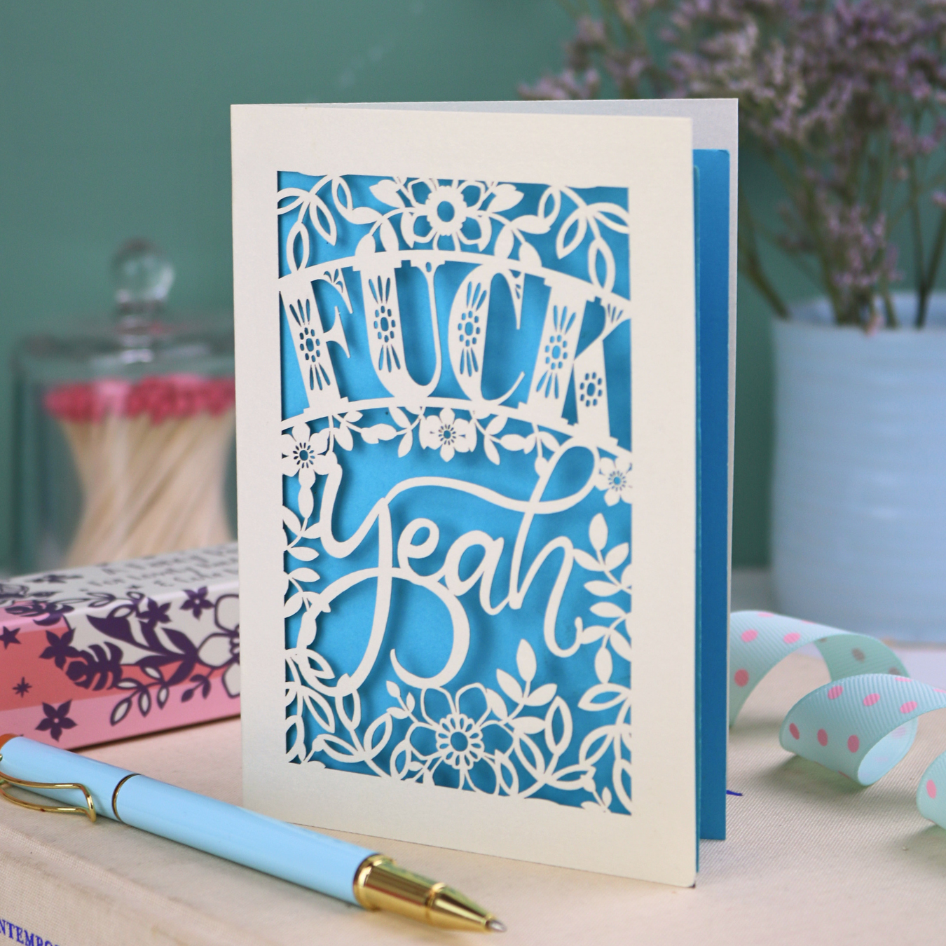 Funny laser cut congratulations Card with decorative, swearing text on a table with stationery items