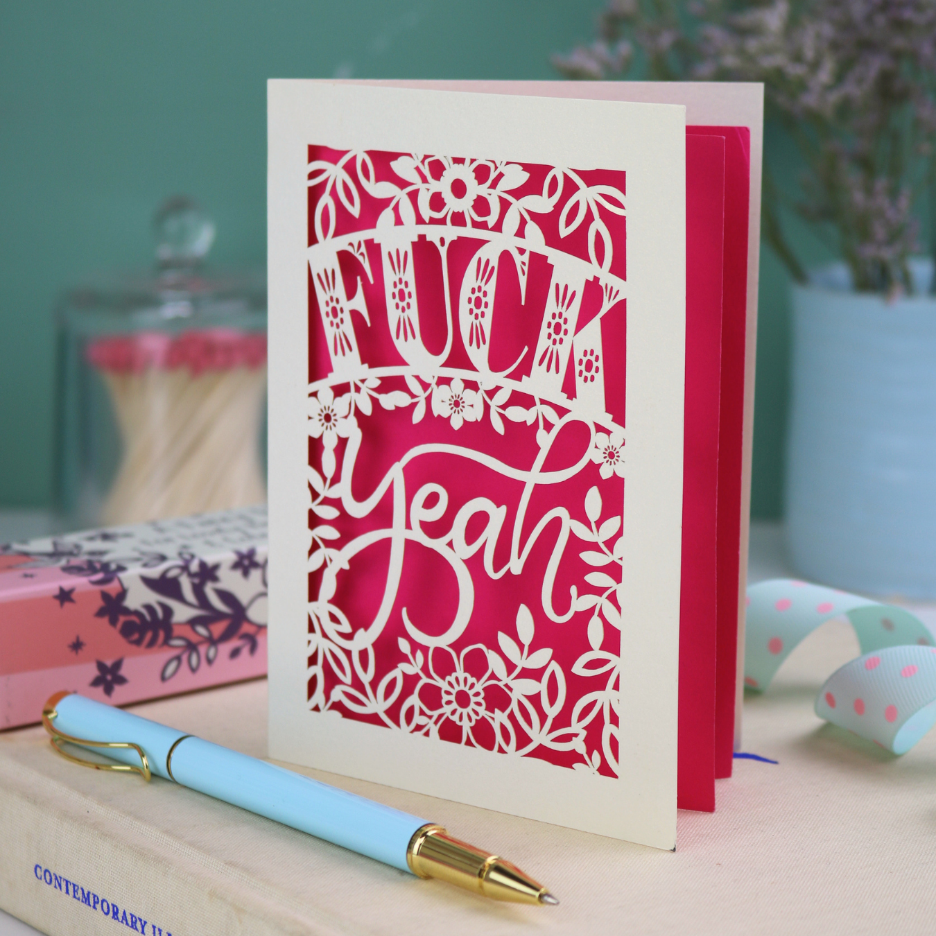 Funny laser cut congratulations Card with decorative, swearing text on a table with stationery items
