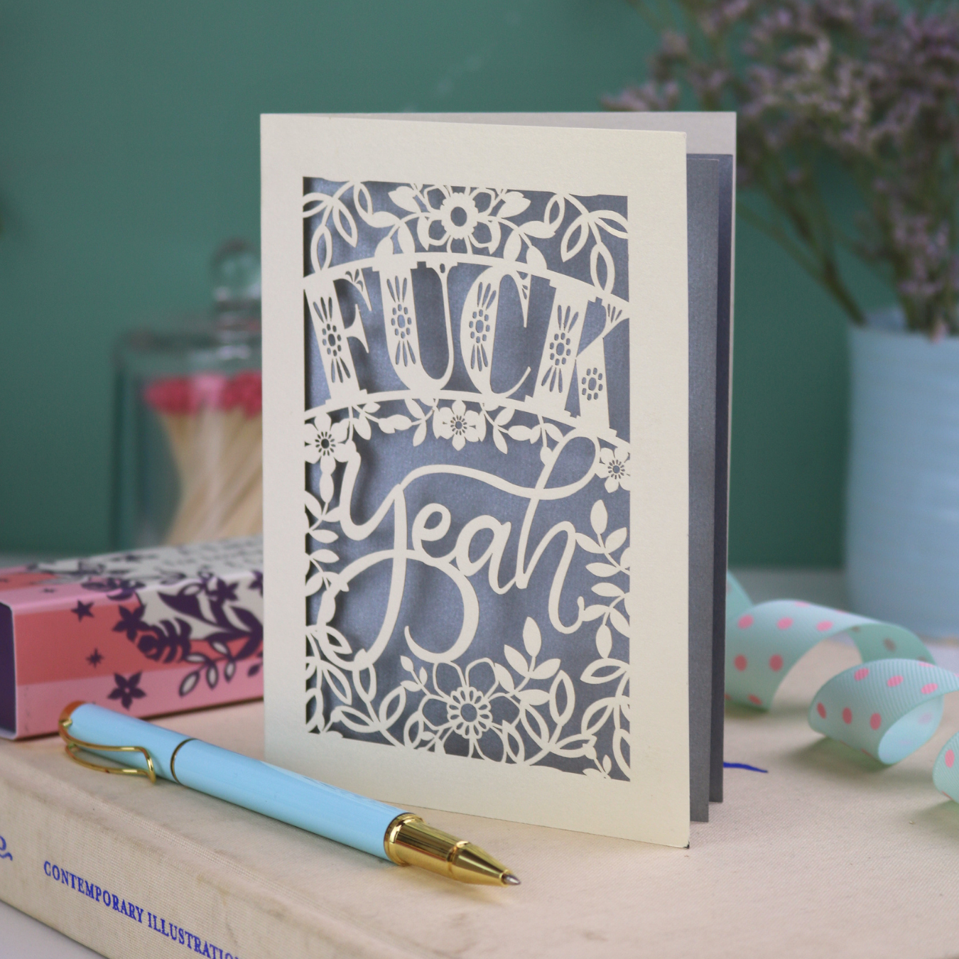 Rude laser cut congratulations Card with decorative, swearing text on a table with stationery items