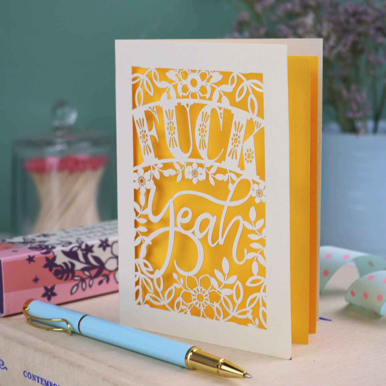 Funny laser cut congratulations Card with decorative, swearing text on a table with stationery items