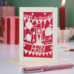 Happy 1st Birthday card with shocking pink and cream design on a table with a pink pen and gift.