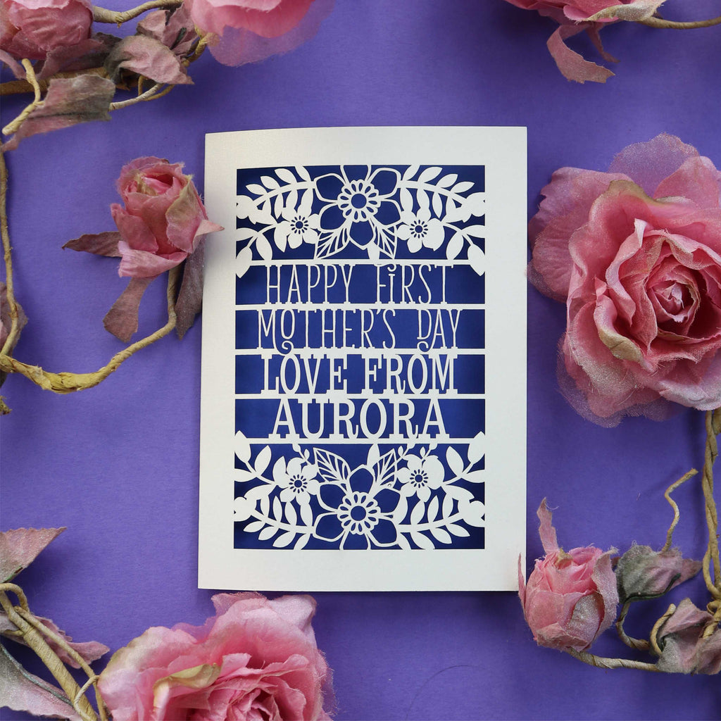 A laser cut 1st Mother's Day card with cut out text that says "Happy First Mother's Day, love from" and is personalised with a name