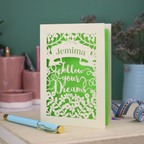 Decorative papercut graduation card with 'Jemima Follow Your Dreams' text on a desk with stationery items.