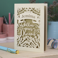 Decorative laser cut graduation card with 'Jemima Follow Your Dreams' text on a desk with stationery items.