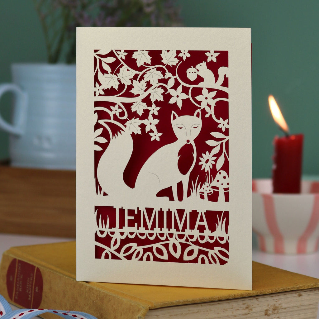 A laser cut fox birthday card with cut out fox illustration and woodland details, personalised with a name underneath the design. 