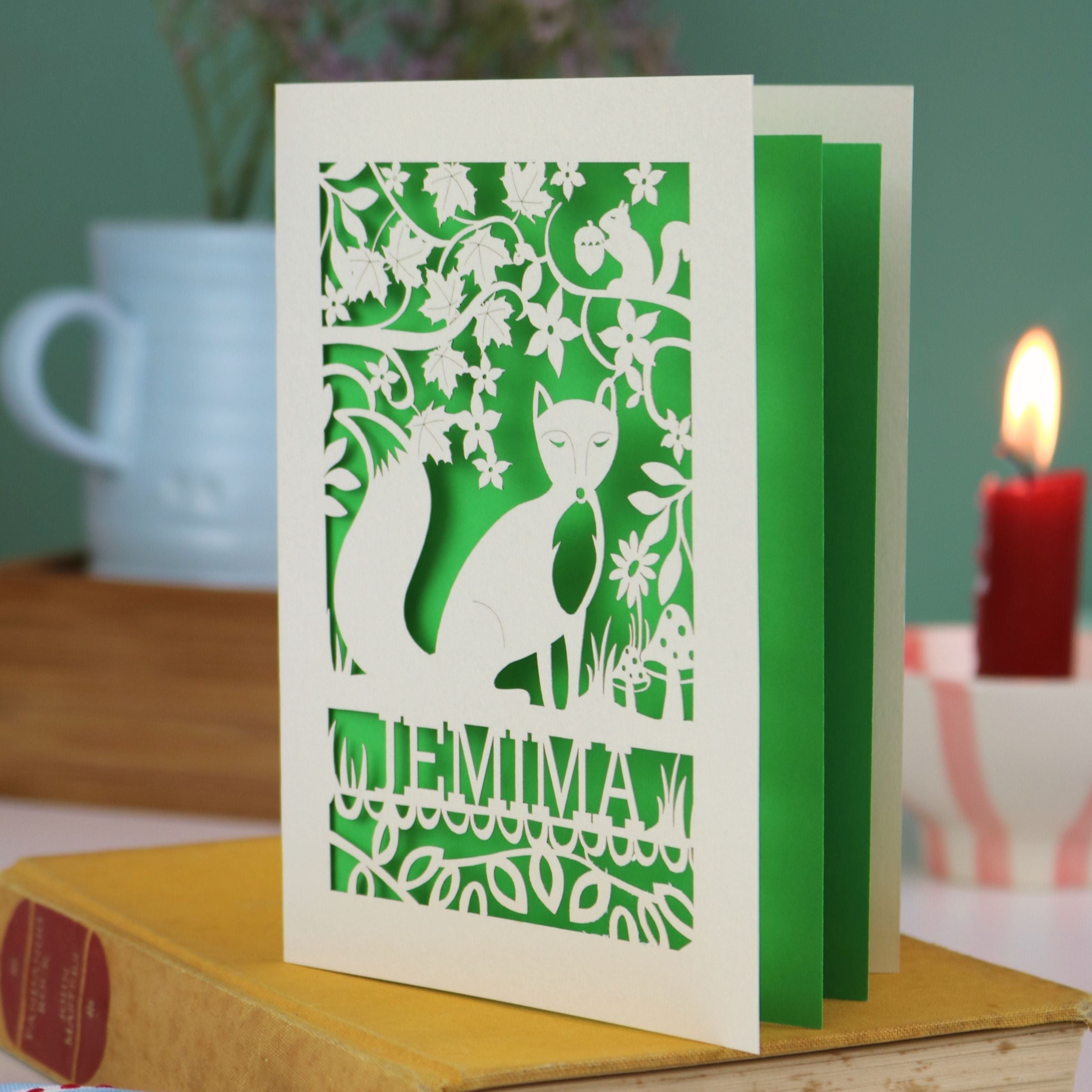 A laser cut fox birthday card with cut out fox illustration and woodland details, personalised with a name underneath the design. 