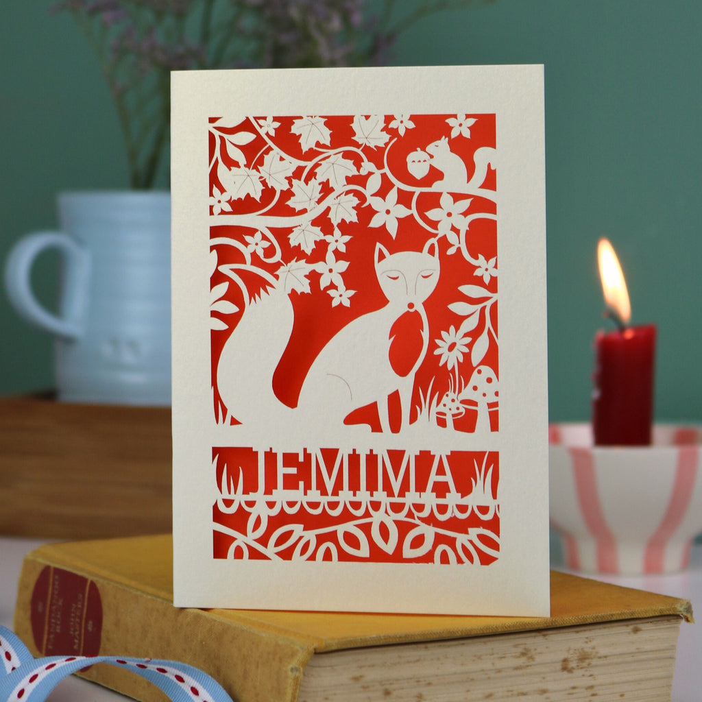 A laser cut fox birthday card with cut out fox illustration and woodland details, personalised with a name underneath the design. 