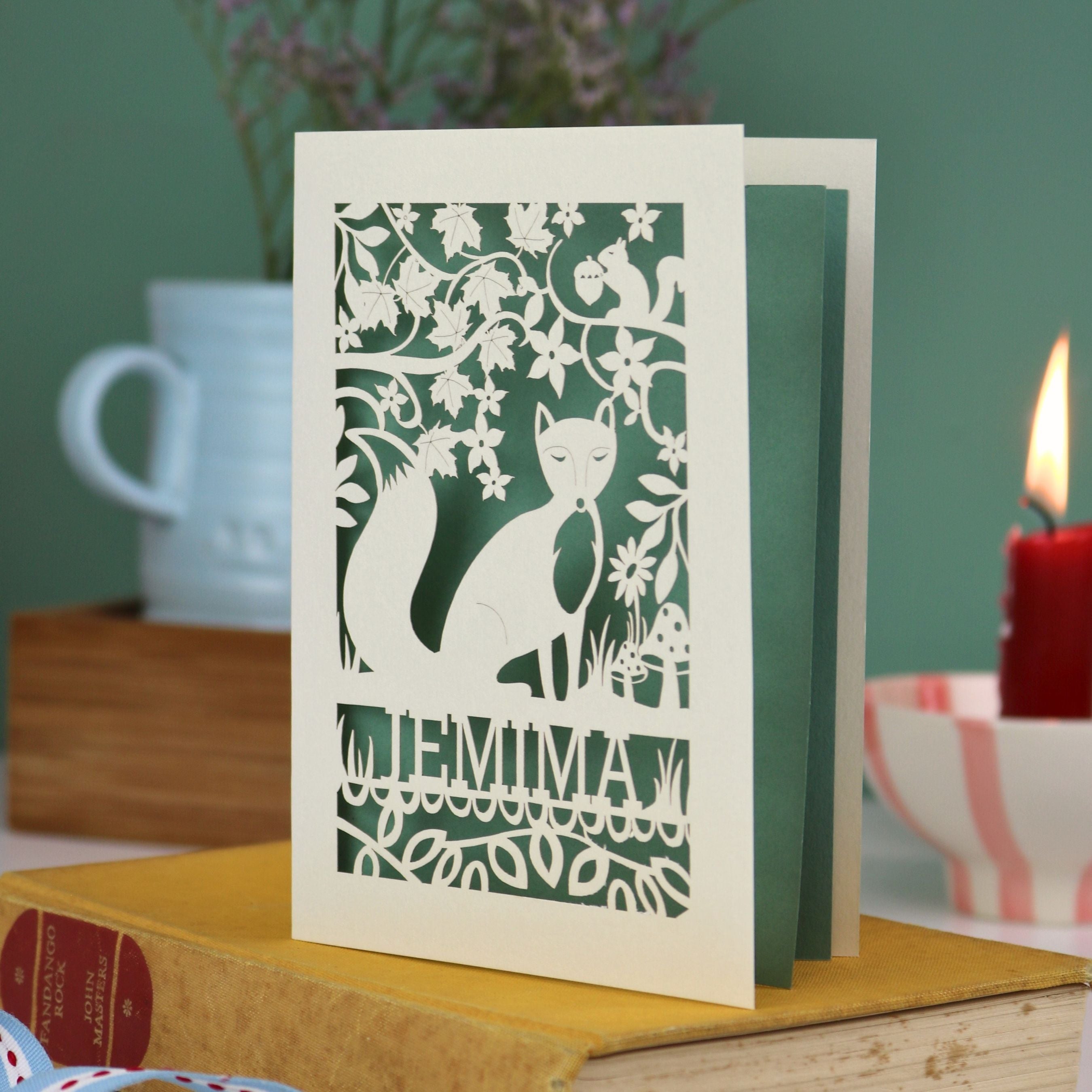 A laser cut fox birthday card with cut out fox illustration and woodland details, personalised with a name underneath the design. 