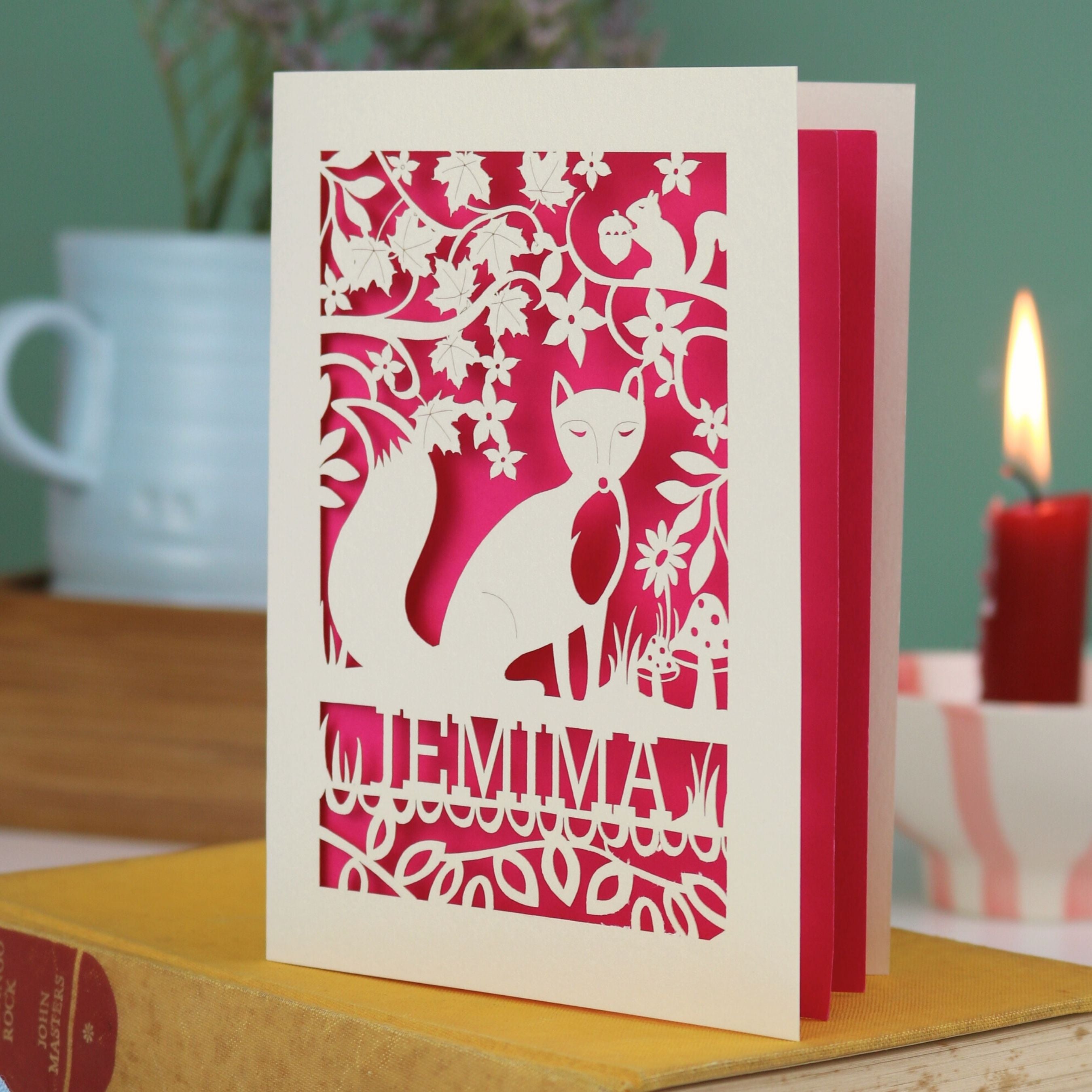 A laser cut fox birthday card with cut out fox illustration and woodland details, personalised with a name underneath the design. 