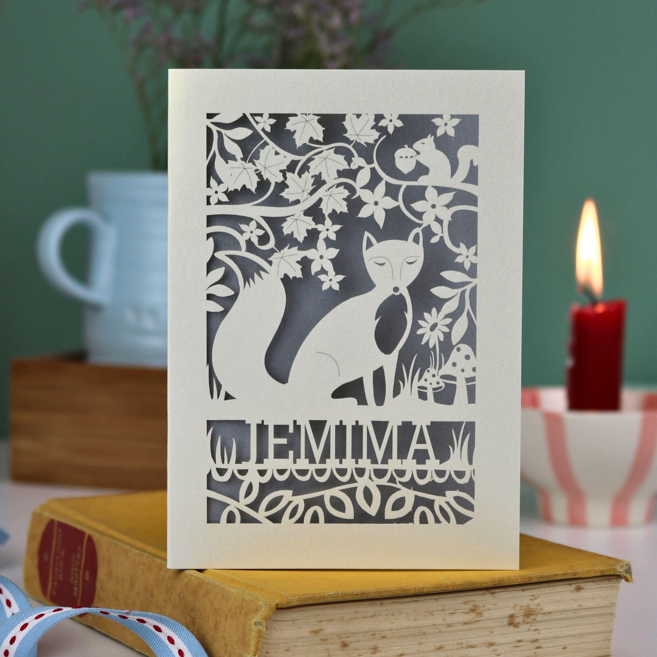 A laser cut fox birthday card with cut out fox illustration and woodland details, personalised with a name underneath the design. 