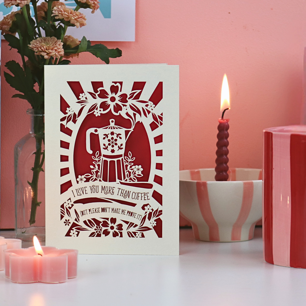 A funny laser cut Valentine's card on desk with candles and flowers, and a pink background