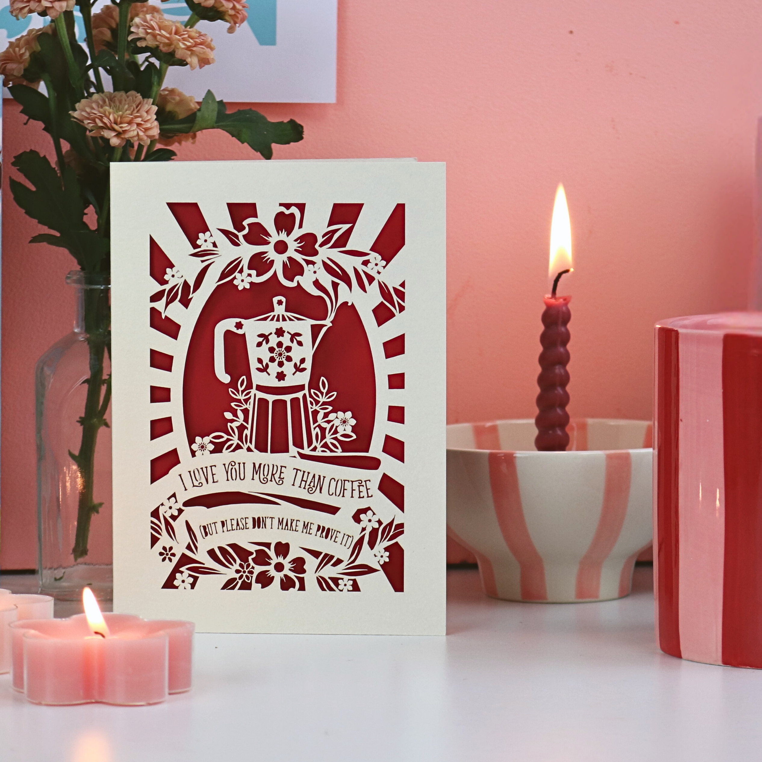 A funny laser cut Valentine's card on desk with candles and flowers, and a pink background