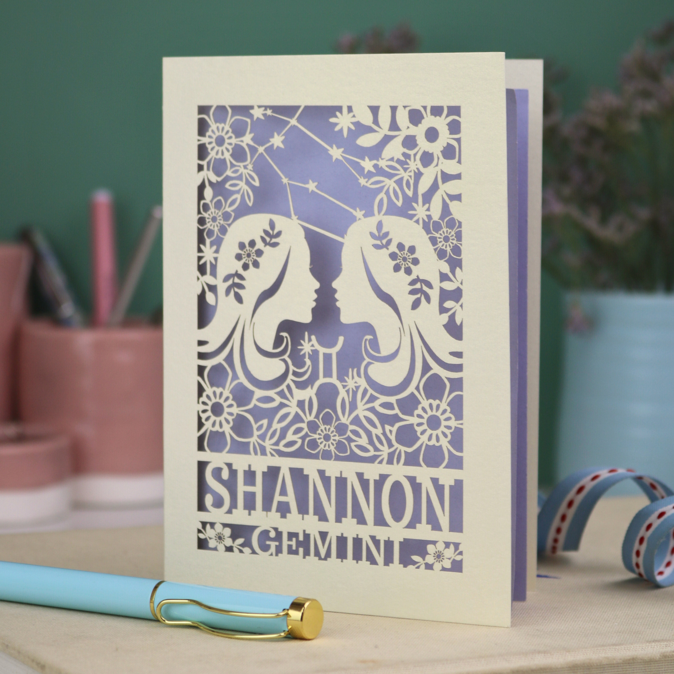 Decorative Gemini Birthday card with laser-cut design and 'Shannon Gemini' text on a desk with stationery items.