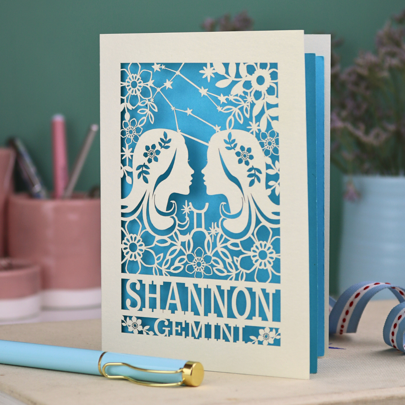 Decorative Gemini Birthday card with laser-cut design and 'Shannon Gemini' text on a desk with stationery items.