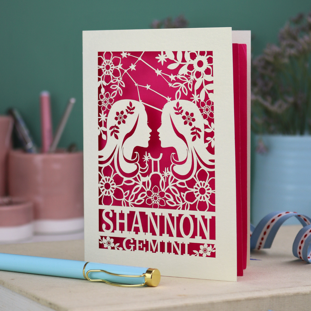 Decorative Gemini Birthday card with laser-cut design and 'Shannon Gemini' text on a desk with stationery items.