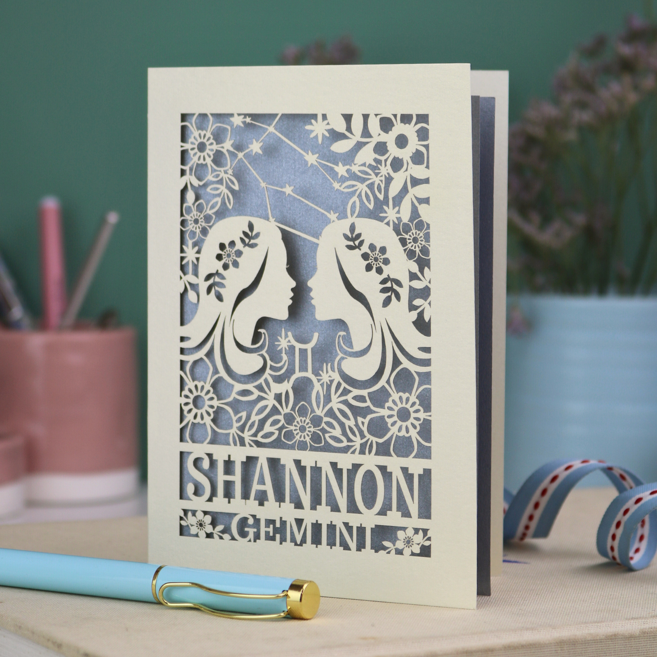 Decorative Gemini Birthday card with laser-cut design and 'Shannon Gemini' text on a desk with stationery items.