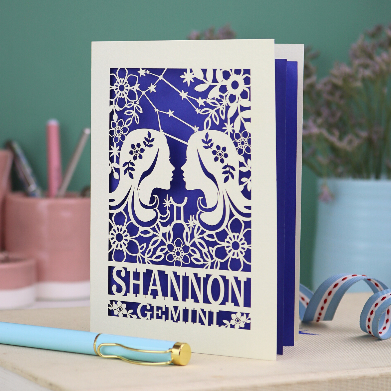 Decorative Gemini Birthday card with laser-cut design and 'Shannon Gemini' text on a desk with stationery items.