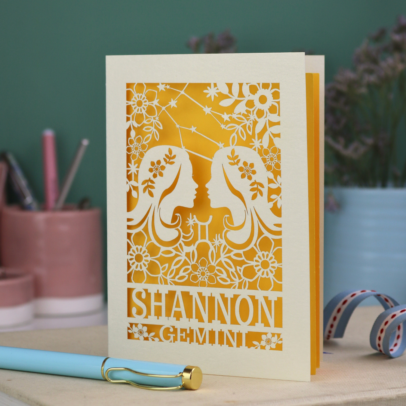 Decorative Gemini Birthday card with laser-cut design and 'Shannon Gemini' text on a desk with stationery items.