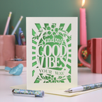 Laser cut Card with 'Sending Good Vibes Your Way' text on a desk with stationery items.