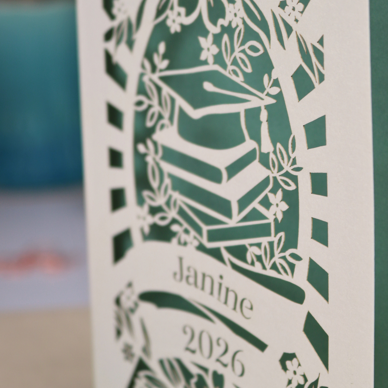 Personalised paper cut graduation card with cap and book design, and personalised with a name and the year in stencil font in a banner