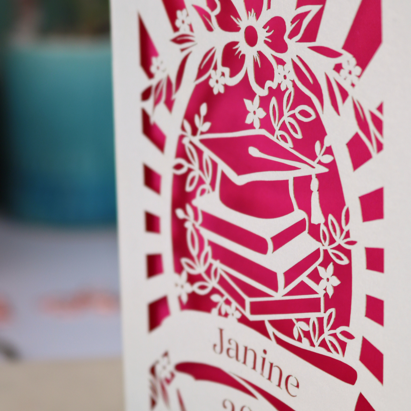 Graduation-themed card with decorative elements and 'Janine' text on a blurred background