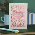 Paper cut Greeting card with floral design and 'Gran' text on a green surface with a pen and mug in the background.