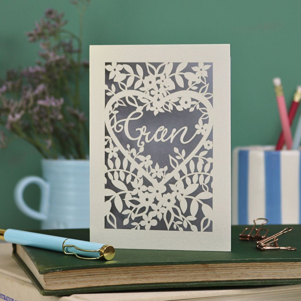 Decorative card with floral design and 'Gran' text on a desk with stationery items.