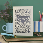 Decorative card with floral design and 'Gran' text on a desk with stationery items.