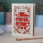 A personalised Valentine's Card with laser cut floral design, personalised with a name cut out in stencil font in a banner, with the text, "Happy Valentine's Day" in a script font.
