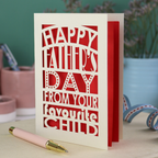 A funny Father's Day card with laser cut text, Happy Father's Day from your favourite child" on a table with a pen and decorative items.