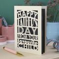 A funny Father's Day card with laser cut text, Happy Father's Day from your favourite child" on a table with a pen and decorative items.